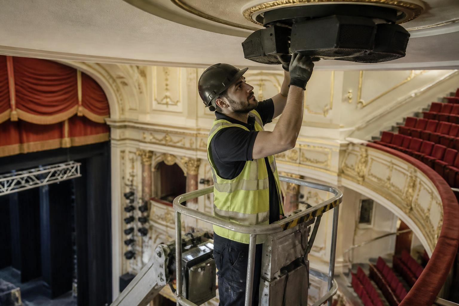 Audio Visual Installers Insurance 2 Sound installer on a mobile platform fitting a ceiling speaker cluster above the stalls of a refurbished UK theatre