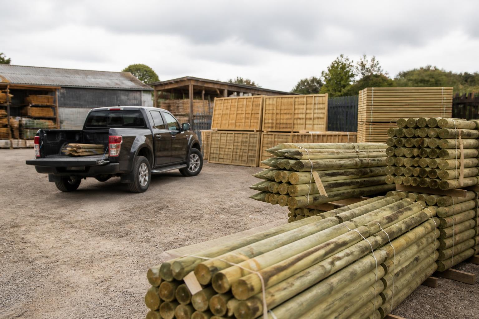 Fencing contractor's yard with stacked treated timber posts, panels and a pickup truck