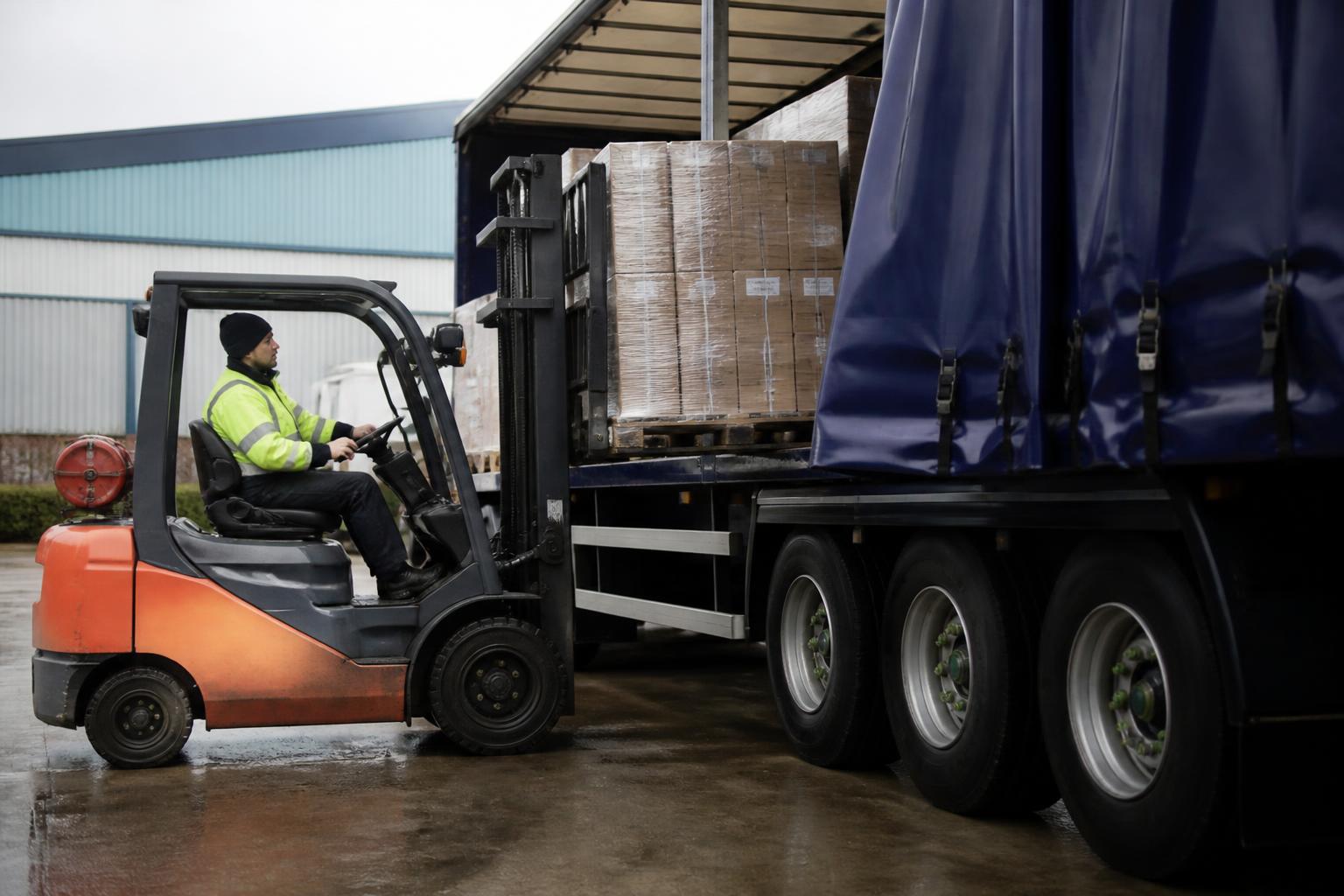 Forklift loading a customer's pallets onto a curtain-sided truck at a UK distribution centre