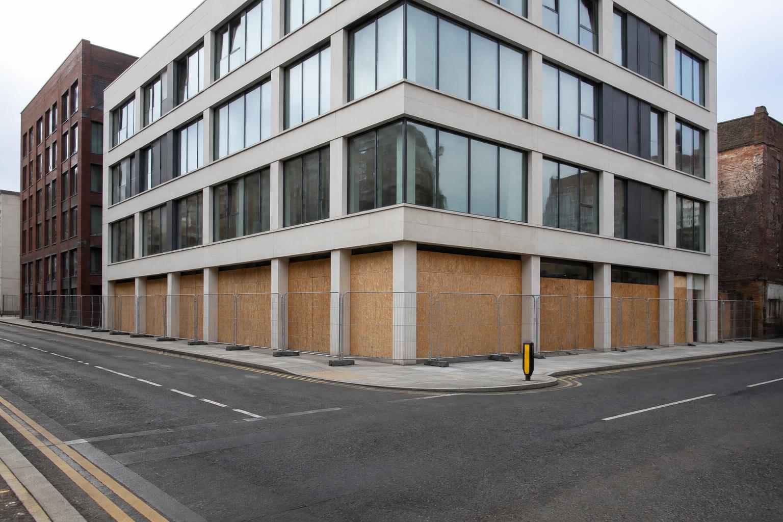 Vacant UK office building with boarded ground floor windows and a security fence